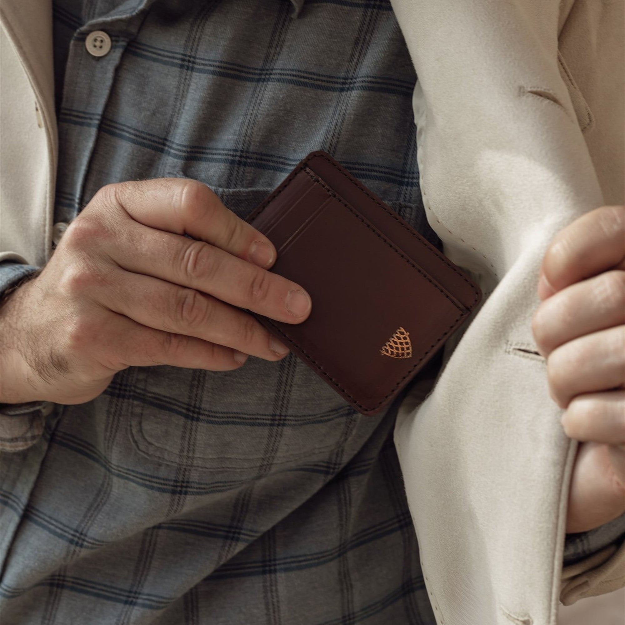 Man tucking the Jefferson Leather Slim ID Wallet in Elderwood Brown into his inside jacket pocket.