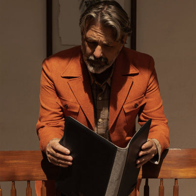 Man in an orange jacket opening the Jefferson Leather Travel Portfolio in Vintage Black.