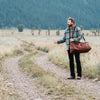 Vintage brown leather duffle bag held by a traveler in a scenic Jackson Hole meadow, highlighting the rugged, stylish design.