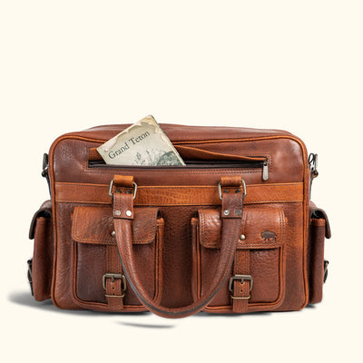 Classic brown leather travel bag with buckled front pockets and a map peeking out, ideal for adventurous, stylish journeys.