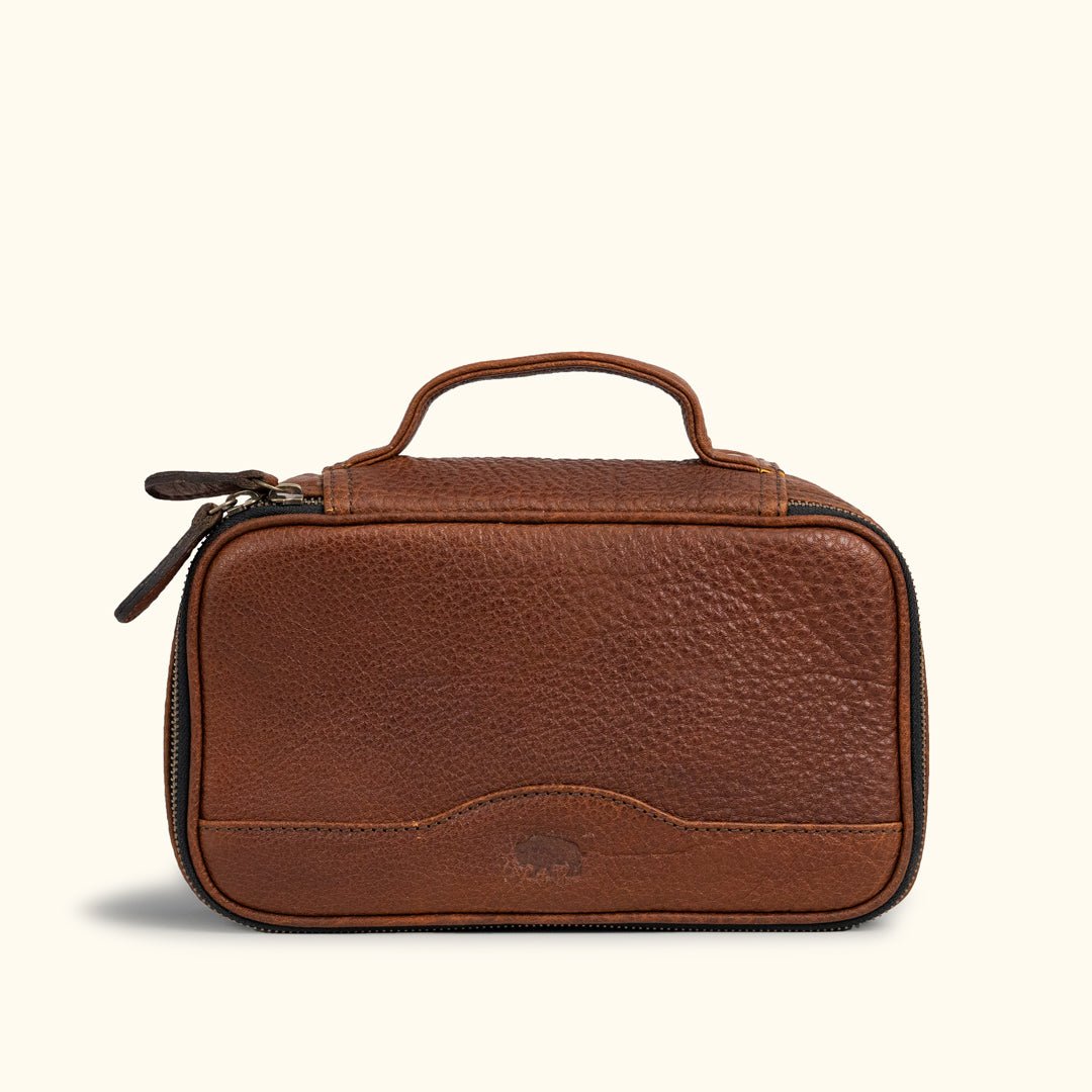 Luxurious brown leather travel pouch with finely stitched detailing, twin zipper pulls, and a solid top handle for sophisticated travelers.