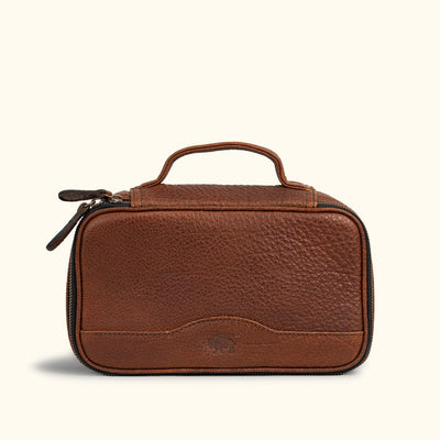 Luxurious brown leather travel pouch with finely stitched detailing, twin zipper pulls, and a solid top handle for sophisticated travelers.