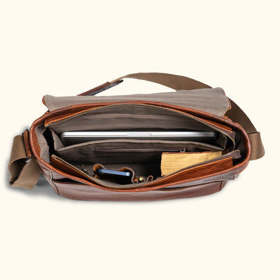 Contemporary tan leather briefcase, long zipper to open the briefcase; computer, phone, book, and pens are pictured inside the briefcase.