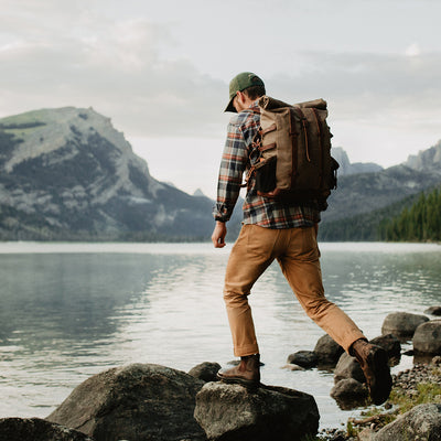 Man with a backpack walking by a lake with mountains in the background