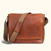 Sleek tan leather messenger bag with wide adjustable canvas strap and smooth finish, perfect for professional and casual use.