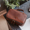 hoverRich brown leather dopp kit placed on a dark marble countertop, partially open to reveal a well-organized interior ideal for sophisticated travel.
