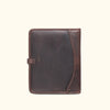 Dark oak leather padfolio with strap closure, perfect for business travel, displayed among travel memorabilia.