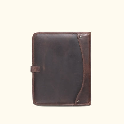 Dark oak leather padfolio with strap closure, perfect for business travel, displayed among travel memorabilia.