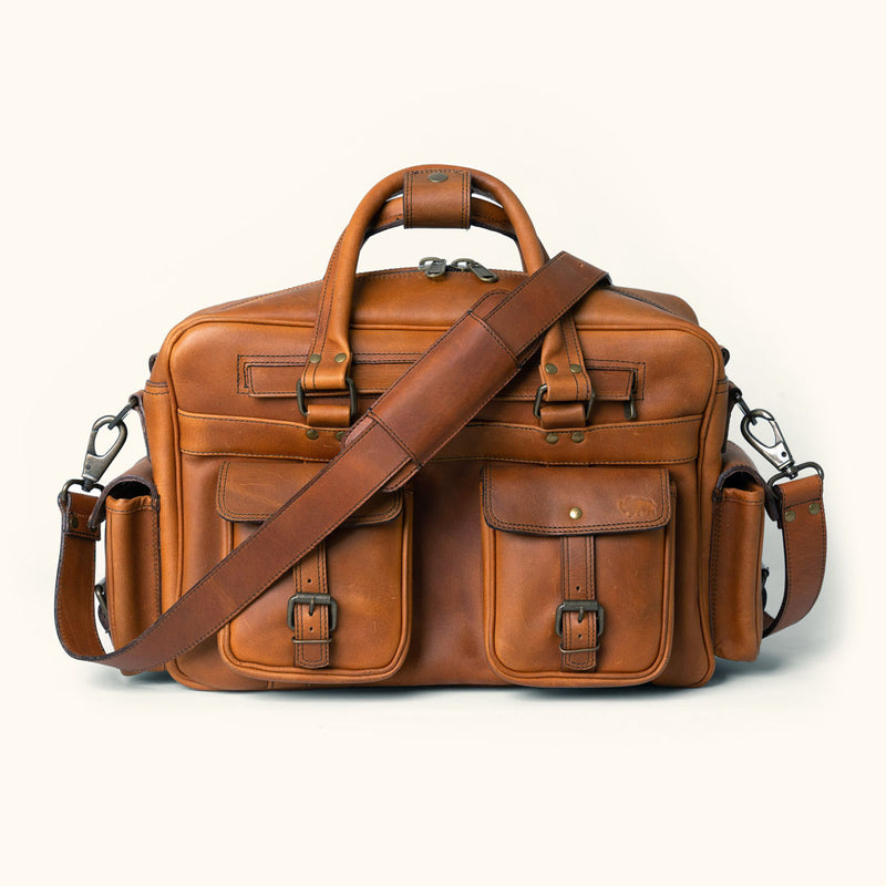 Amber brown Roosevelt buffalo leather pilot bag featuring multiple pockets, adjustable straps, and durable metal hardware.