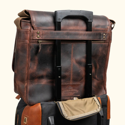Robust dark brown leather travel bag attached to a suitcase handle, featuring a long zipper pocket on the back for added convenience.