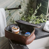 Open brown leather dopp kit on a marble countertop displaying grooming essentials, set against a backdrop of lush green plants in a stylish bathroom.