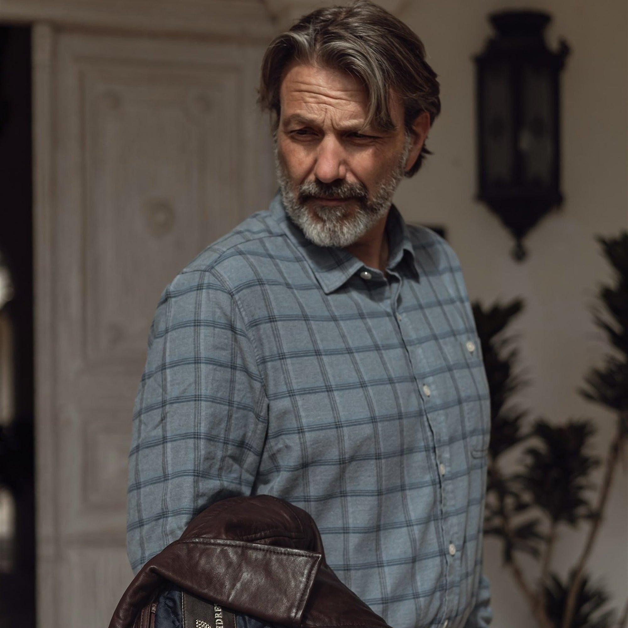 Man in the Windsor Cotton Shirt in Sky Pane carrying a leather jacket through a courtyard
