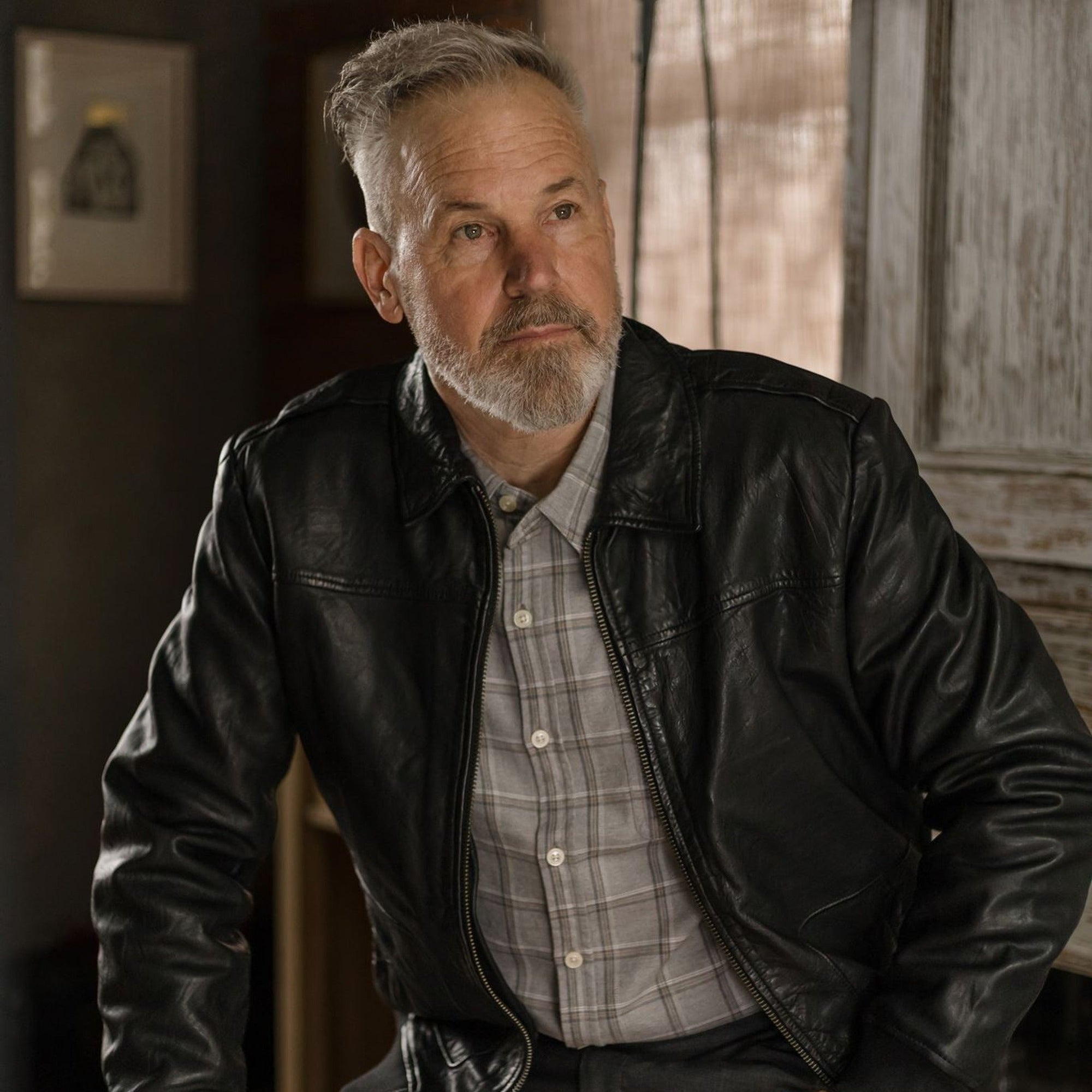 Seated man in the Windsor Cotton Shirt in Stone Pane and a black leather jacket