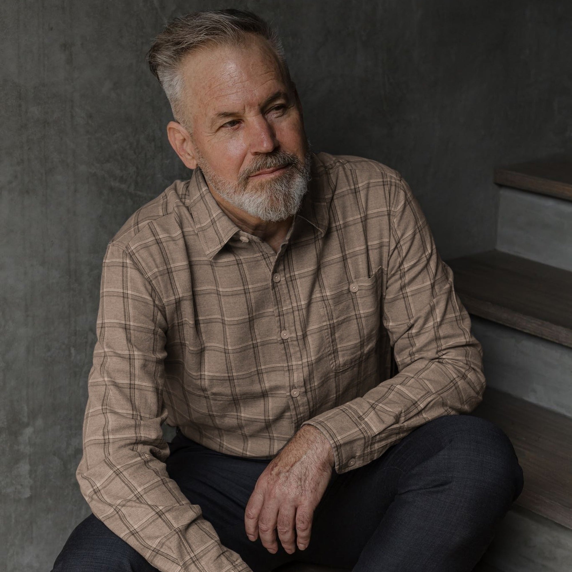 Man in the Windsor Cotton Shirt in Timber Pane, seated against a concrete wall
