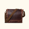 Elegant dark oak brown leather satchel with a wide, adjustable canvas strap, showcasing a smooth, well-worn patina and classic design.