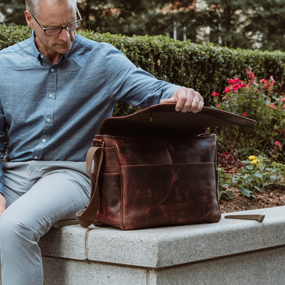Durable dark oak leather satchel with easy access flap, perfect for securely carrying laptops and documents.