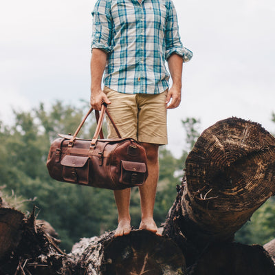 Man hikes with a durable leather duffle, perfect for outdoor activities, featuring adjustable straps and a robust build.