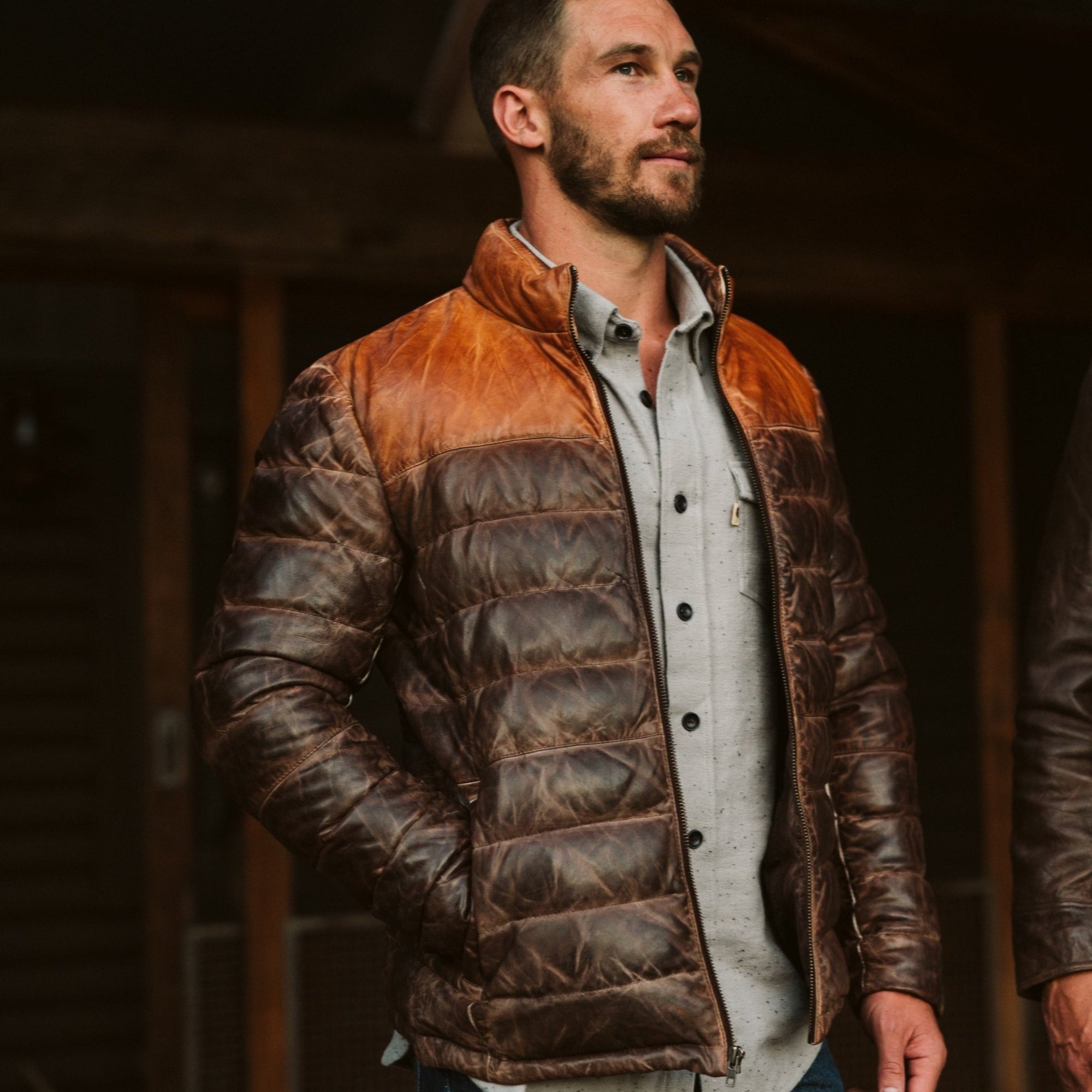 Man wearing a brown leather puffer jacket with a contrasting collar, standing outdoors with a confident expression.
