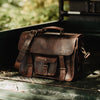 Rugged Men's Leather Briefcase Bag in Dark Oak sitting in a truck bed, showcasing vintage design with sturdy buckles and shoulder strap.