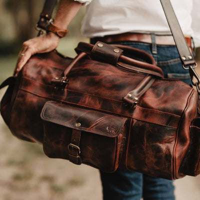 Premium buffalo leather travel duffle bag in dark oak, equipped with multiple pockets and a cross-body strap for convenience and style.
