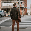 Modern man crossing a busy street, stylishly dressed in a tweed jacket and carrying a vintage dark brown leather messenger bag.