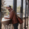 Man in brown jacket and cap carrying an amber brown leather Roosevelt satchel messenger bag, with adjustable strap.