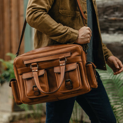 Man walking with a Roosevelt buffalo leather pilot bag in amber brown, emphasizing its utility and fashionable design.