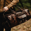 Traveler with dark brown leather duffle bag featuring ample storage, secure straps, and a rugged outdoor-ready design.