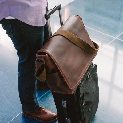 Large dark oak leather satchel with wide strap, perfect for secure attachment to luggage during travel.