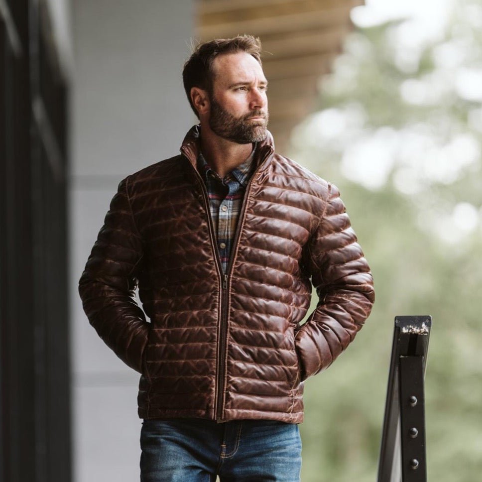 Man wearing the Bridger leather down jacket in dark brown outside a cabin