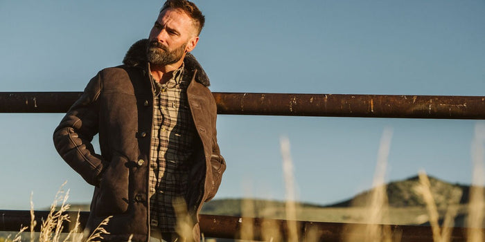 Man in the Durango Shearling Barn Coat in Espresso Brown leaning on a ranch fence at golden hour