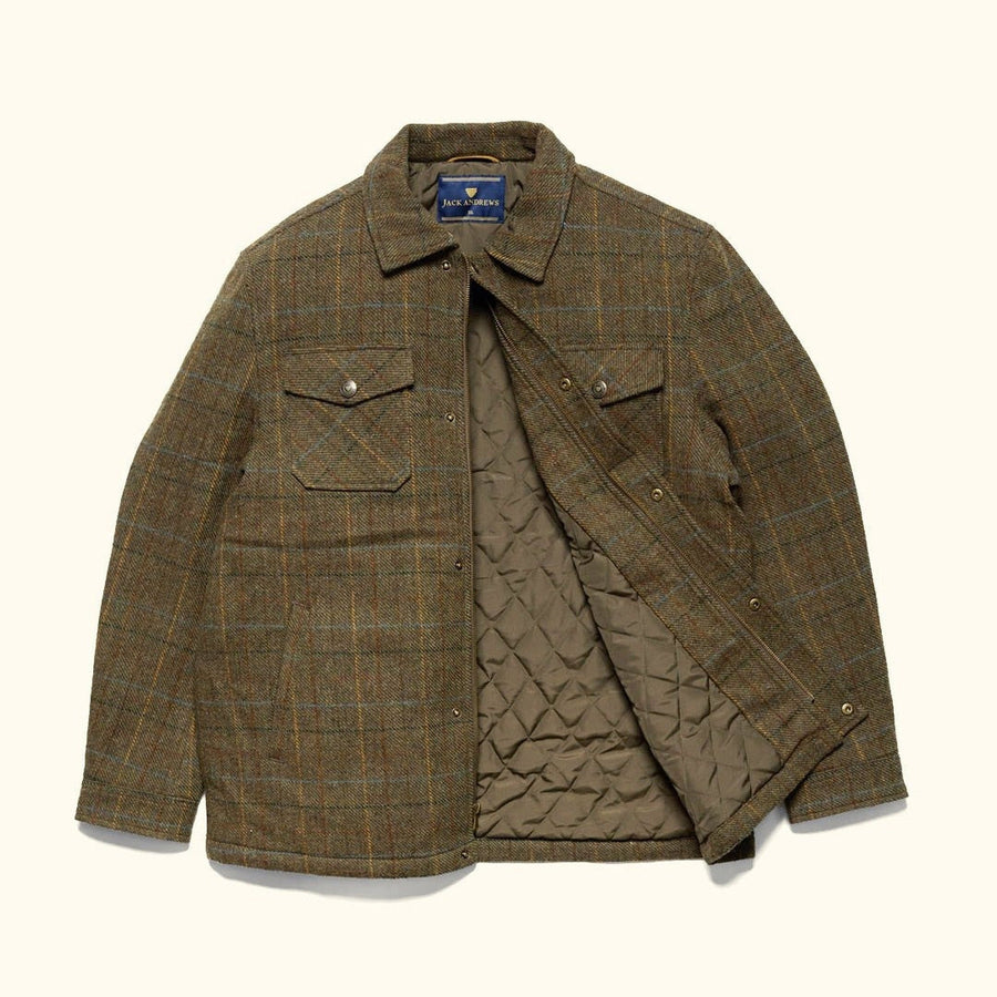 Man in the Aberdeen Wool Jacket in Fir Heather seated on a wooden bench by an outdoor fire
