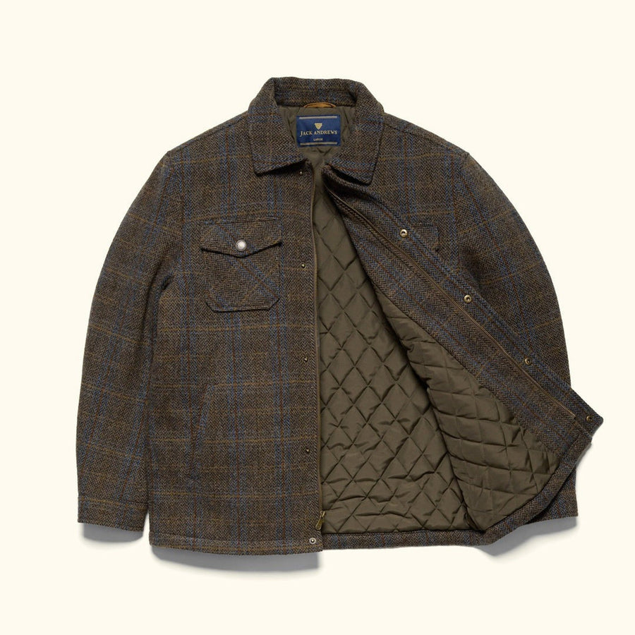 Gray-haired man in the Aberdeen Wool Jacket in Thistle Bark Plaid seated against a sunlit stucco wall with a leather bag