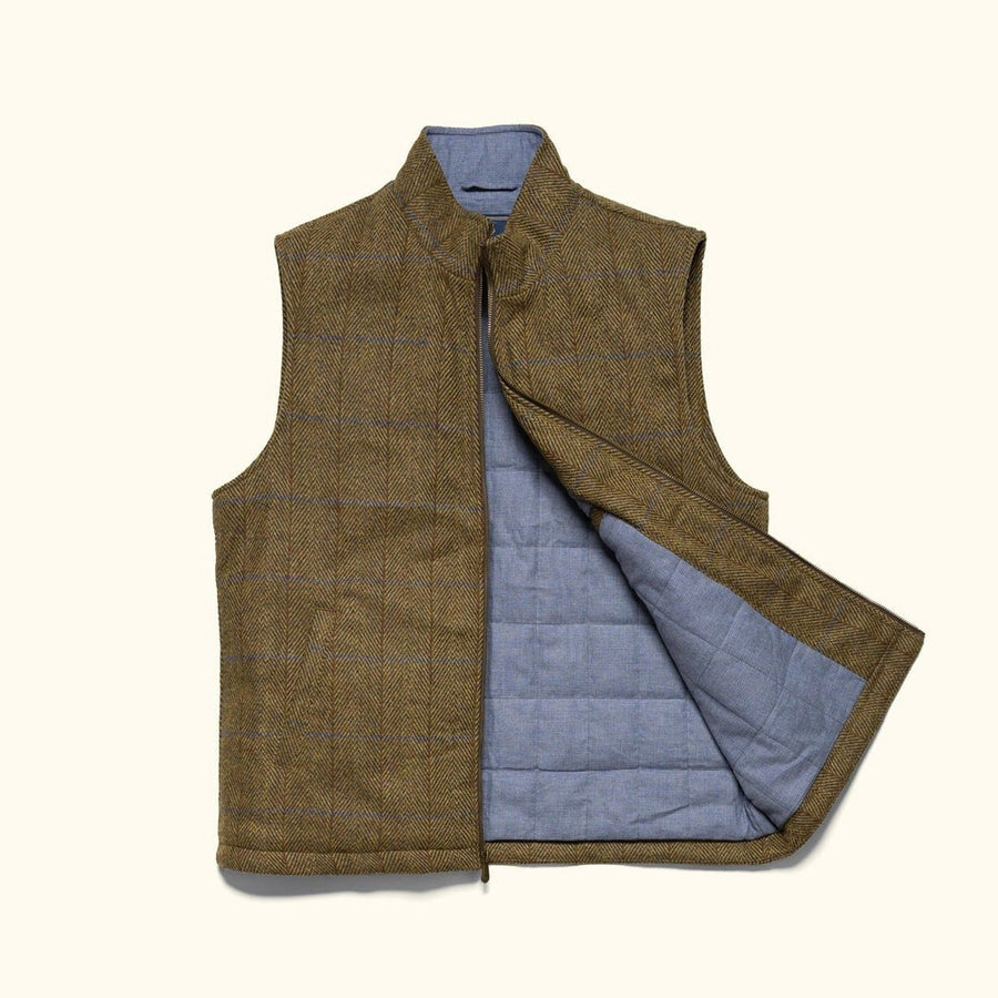 Man in the Ashton Wool Herringbone Vest in Mosswood over a cream cable-knit sweater on a terrace