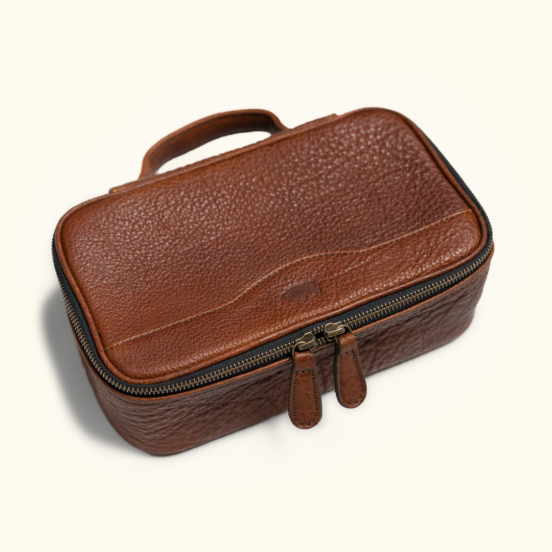 Compact brown leather dopp kit with textured finish, sturdy handle, and dual zipper pulls, perfect for organized travel essentials.