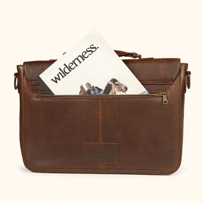 Brown leather bag with a 'wilderness' magazine inside on a white background
