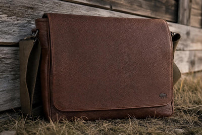 Satchel Brown leather bag leaning against a wooden wall with a rustic outdoor setting.