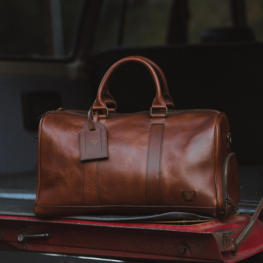 Premium tan leather weekender bag with spacious interior, reinforced stitching, and stylish brand logo.