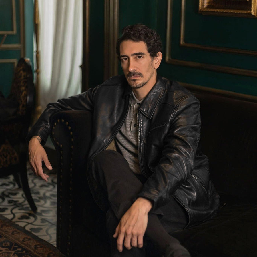 Man seated in the Glenwood Leather Driving Jacket in Vintage Black in a green-walled sitting room.