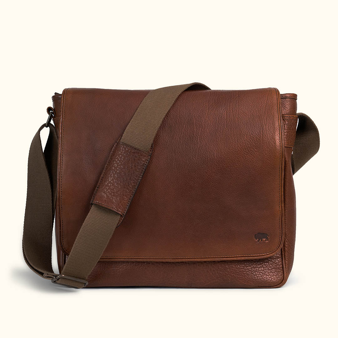 A brown full grain leather messenger bag with a structured body and a shoulder strap.
