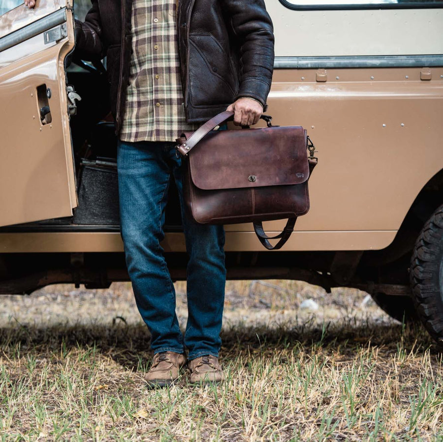 Vintage dark brown leather messenger bag with aged patina, featuring sturdy handle, adjustable strap, and classic front buckle closure.