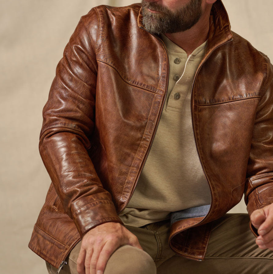 Man wearing a brown leather jacket over a green shirt on a beige background