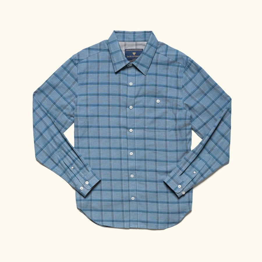 Man in the Windsor Cotton Shirt in Sky Pane carrying a leather jacket through a courtyard