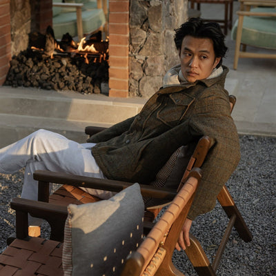 Man in the Aberdeen Wool Jacket in Fir Heather relaxing in a wooden sling chair by the fire