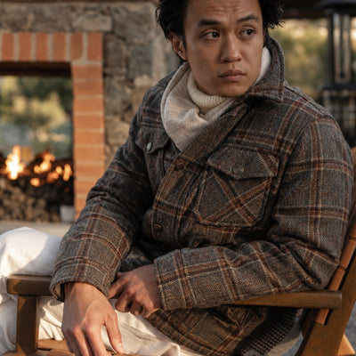 Man in the Aberdeen Wool Jacket in Grey Briar and a scarf seated by an outdoor fire