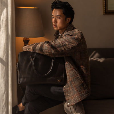 Man in the Aberdeen Wool Jacket in Grey Briar seated by a window with a leather bag