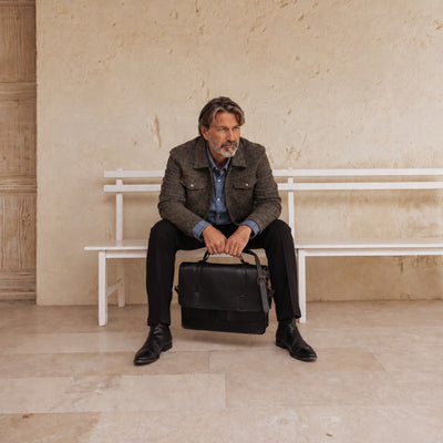 Gray-haired man in the Aberdeen Wool Jacket in Thistle Bark Plaid seated on a white bench with a leather briefcase
