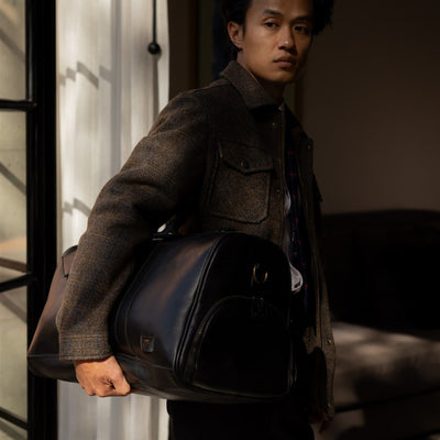 Man in the Aberdeen Wool Jacket in Thistle Bark Plaid in a doorway with a leather bag