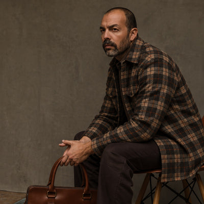 Man in the Aberdeen Wool Twill Shirt Jac in Brown Briar seated on a stool with a leather briefcase