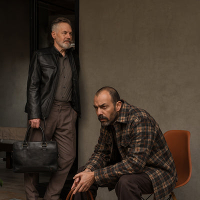Seated man in the Aberdeen Wool Twill Shirt Jac in Brown Briar with a leather briefcase, a man in a black leather jacket behind